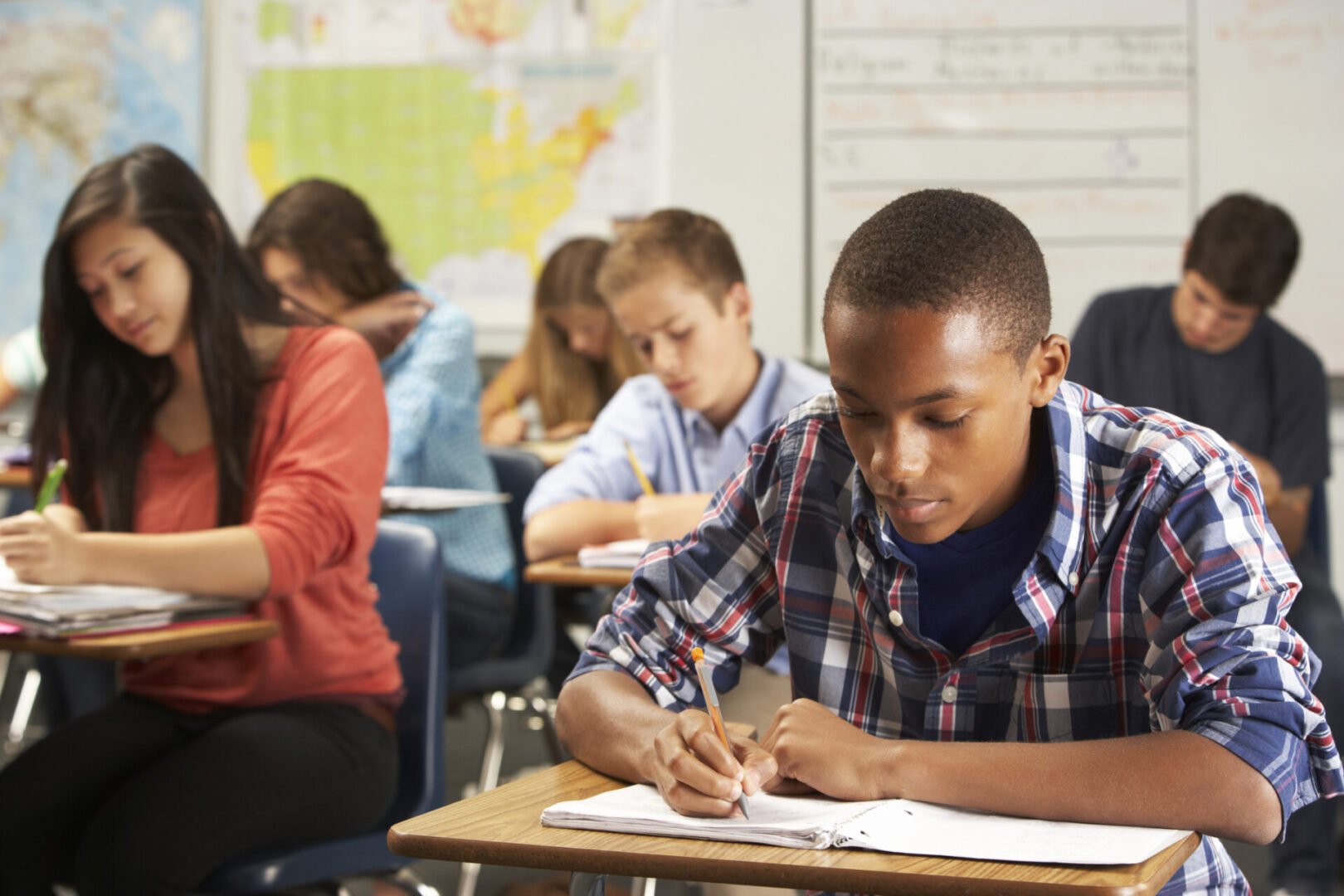 Male student in classroom writing in notebook Students writing in a classroom setting.